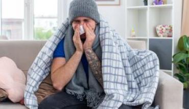 young-ill-man-wearing-scarf-winter-hat-wrapped-blanket-sitting-sofa-living-room-wiping-nose-with-napkin-with-closed-eyes_0.jpg